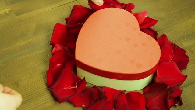 Girl lays out a heart on a wooden table from rose petals. Time laps