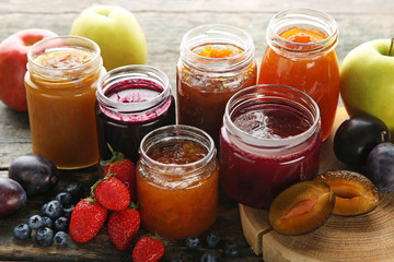 Glass jars with different kinds of jam on wooden table