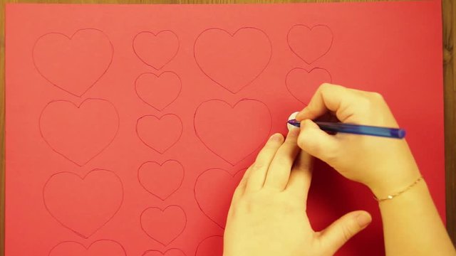 The girl draws on a red cardboard hearts. Close-up