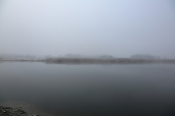 Thick morning fog over a narrow river in winter
