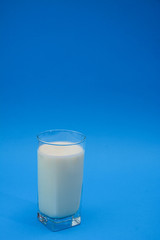 Milk in a glass with a blue pastel background. Healthy eating concept. Glass of milk isolated on blue. Vertical.