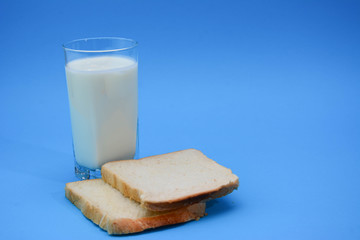 A glass of milk with a toasted bread on a pastel blue background. Two Bread Slices on blue background. Natural healthy food and organic farming concept. Copy space.