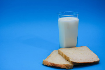 A glass of milk with a toasted bread on a pastel blue background. Two Bread Slices on blue background. Natural healthy food and organic farming concept. Copy space.