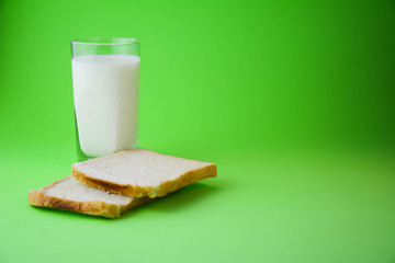 Natural healthy food and organic farming concept. A glass of milk with a toasted bread on a pastel green background. Two Bread Slices on green background. Copy space. Horizontal.