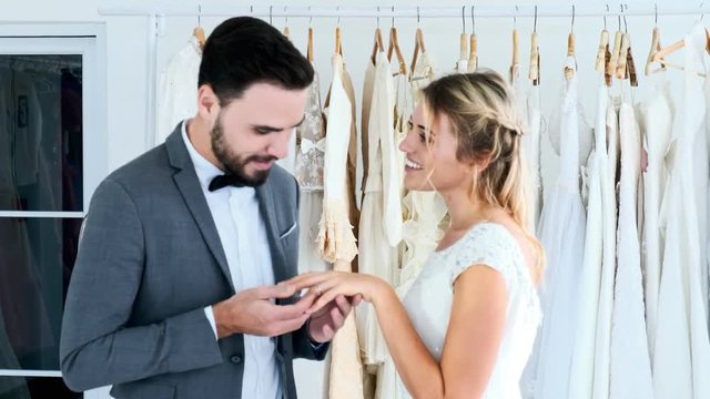 Romantic wedding couple in expensive dress shop. White man and woman in bride dress, man putting ring to his future wife. Romantic young couple concept.