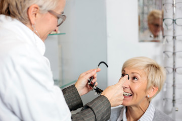 Smiling senior woman having eyesight exam and diopter measurement at the ophthalmology clinic....
