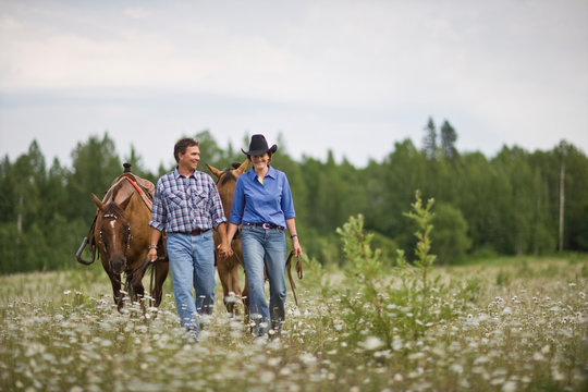 Mature couple leading horses through a meadow