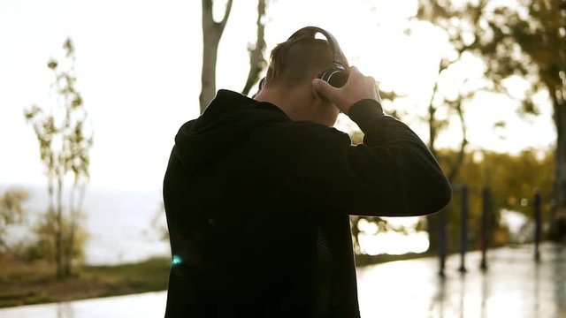Sport, fitness, young muscular man working out during a workout on the street.Caucasian athlete puts on headphones and starts making deep push ups on paralel bar. Morning