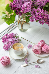 Bouquet of lilacs, cup of coffee, homemade marshmallow. Romantic spring morning. Selective focus