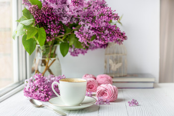 Bouquet of lilacs, cup of coffee, homemade marshmallow and stack of books. Romantic spring morning. Selective focus