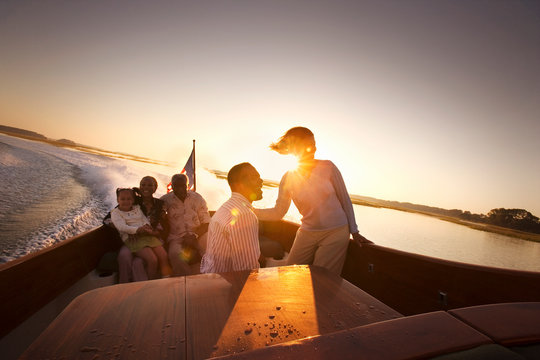 Mature adult couple sitting with a mid-adult couple and their young daughter on a boat at sunset.