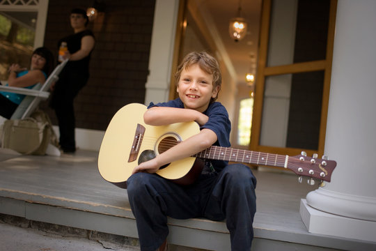 Portrait of a boy holding an acoustic guitar while sitting on a porch step.