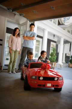 Smiling young girl and her brother sitting in a small red car given to her by her parents.