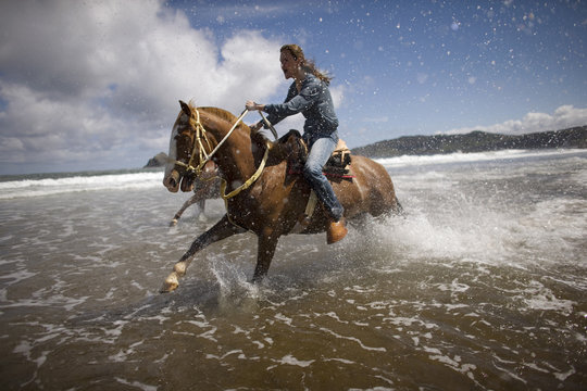 Young woman horseback riding at a beach.