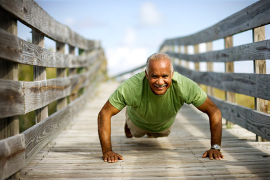 Portrait of a mature adult man doing push ups along a wooden path.