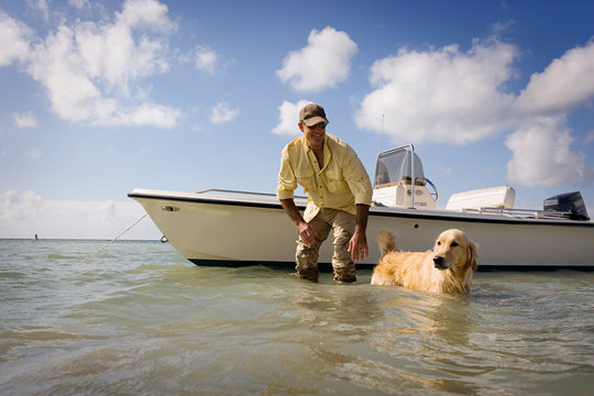 Smiling man standing next to his boat in shallow water with his dog.