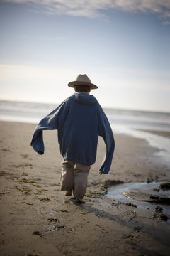 Young boy wearing a hat and baggy sweater on the beach.