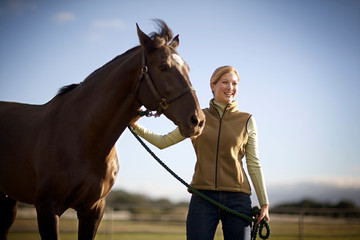 Young adult girl standing with a horse in a field.