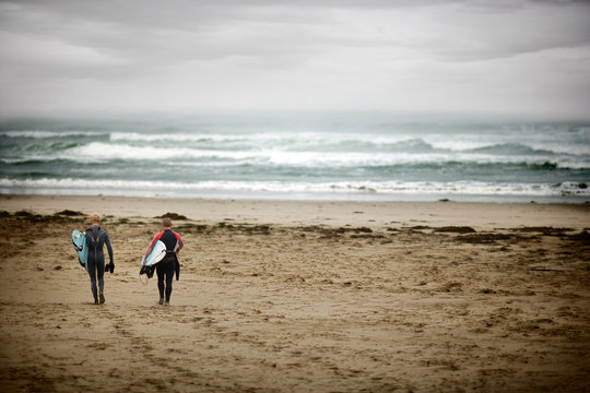 Two teenage boys holding surfboards walking across a beach.