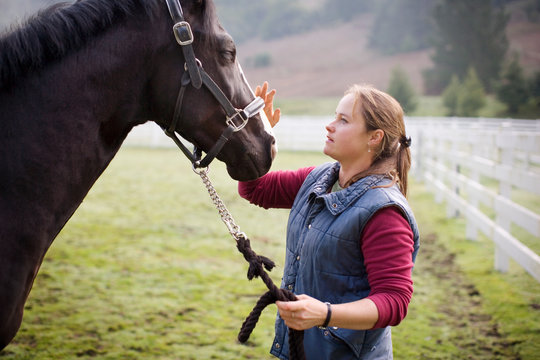 Young woman standing in a paddock with her horse.