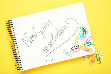 New year resolution in notepad with paper clips on yellow background