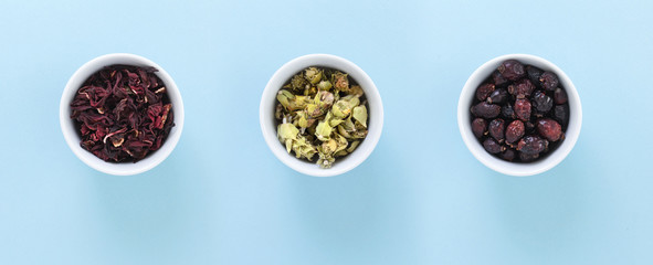 Three white bowls with Hibiscus, Ironwort and Wild rose tea, on blue background.