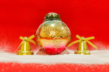 Colorful christmas ball  between two golden bells covered with snow on a red background