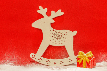 White reindeer and gift boxes in the snow on a red background