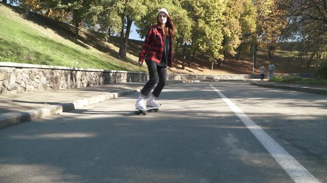 Cute skateboarder girl in a white hat and a plaid shirt rides a skateboard outdoors. Hipster girl riding skate board Hobbies and lifestyle