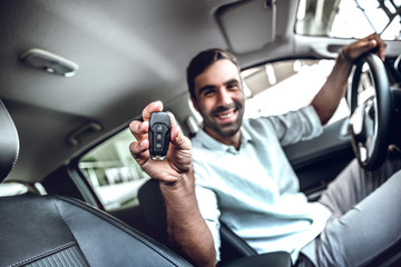 Handsome young man showing a car key inside his new vehicle