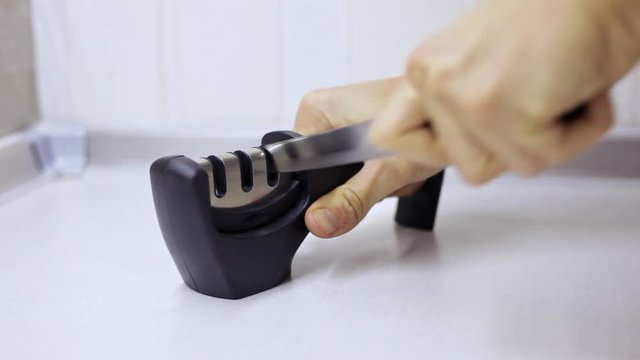 Manual sharpening of a knife in a special sharpener in a kitchen, man hands with knife in close-up