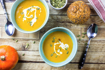 Roasted pumpkin and carrot soup with cream and pumpkin seeds on wooden background. Top view. Copy space