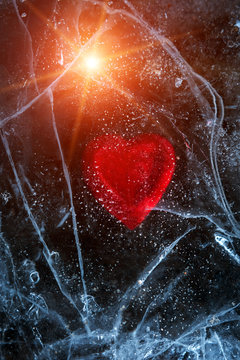 frozen red heart in blured ice . abstract winter background at sunst.