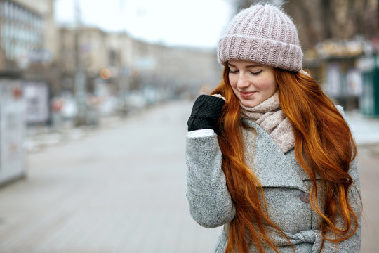 Closeup Shot Of Amazing Ginger Model With Long Hair Wearing Knitted Cap And Scarf Walking At The City. Empty Space