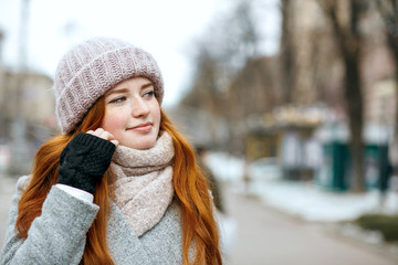 Closeup portrait of attractive ginger girl with long hair wearing warm clothes walking at the city. Empty space