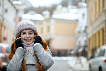 Adorable red haired woman wearing warm winter clothes walking down the street. Empty space