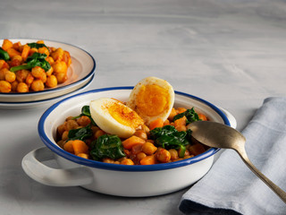 Spanish cuisine. Chickpea and spinach stew with eggs on light gray background. 