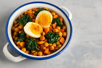 Spanish chickpea and spinach stew with eggs on light gray background. Spanish cuisine.