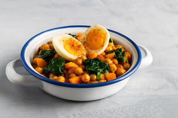 Mediterranean chickpea and spinach stew with eggs on light gray background. Spanish cuisine.