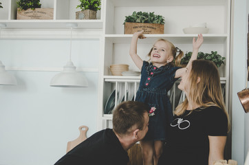 young family with pregnant woman and little girl sitting in scandinavian kitchen and having fun