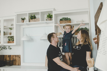 young family with pregnant woman and little girl sitting in scandinavian kitchen and having fun