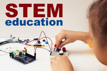 A cute girl constructs robot arduino and program it. The boards and microcontrollers are on the table. STEM education inscription. Programming. Mathematics. The science. Technologie. DIY. 