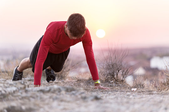 Handsome young man doing push up exercise on the field.