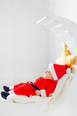 A profile of a baby in a suit of Santa Clause who is lying on th