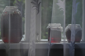 Jar, jars of jam with red currants standing on the windowsill in the farmhouse. View of the garden.