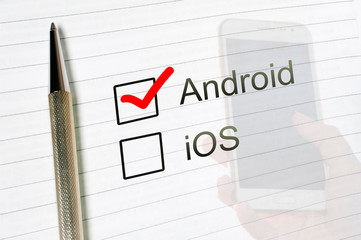 Android choice or iOS text, marked check box with a pen on lined paper smartphone hand background. UI questionnaire concept