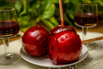 Red candy apple on ceramic plate and glass of cherry liqueur. Wooden table and home liana vine in the background.