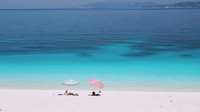 Video shot of amazing beach on mediterranean sea. Tourist chilling on the most beautiful white pebble beach with clear azure emerald sea water. Summer vacation lifestyle concept