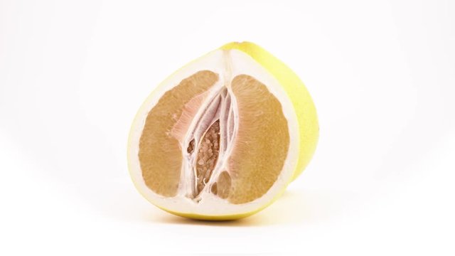 Two halves of yellow pomelo citrus fruit rotating on the turntable. Cross section cut. Isolated on the white background. Close-up. Macro.
