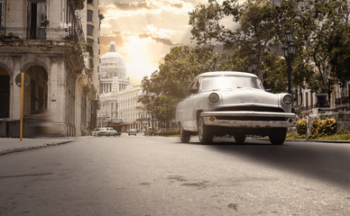 Old classic american taxi rushing through the streets of Havana Cuba with the Capitol and sunset in the background.
